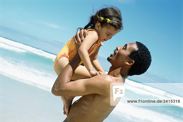 Mann hält Tochter am Strand hoch  Seitenansicht
