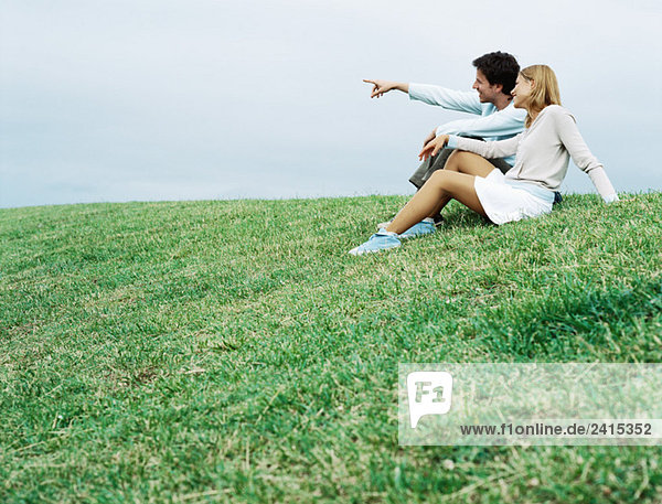 Paar sitzt auf Gras und schaut in die Ferne.