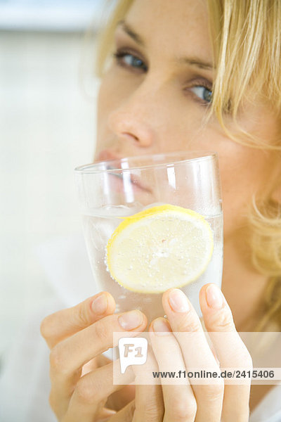 Frau hält ein Glas kohlensäurehaltiges Wasser mit Zitronenscheibe