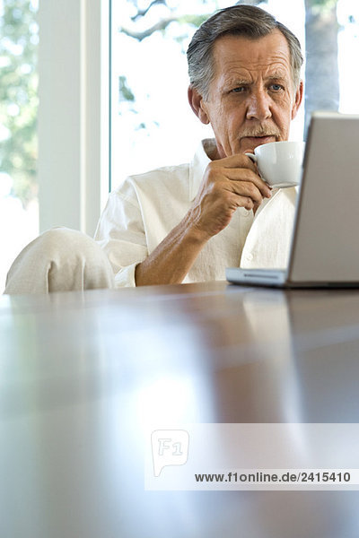 Senior Mann trinkt Kaffee und benutzt Laptop