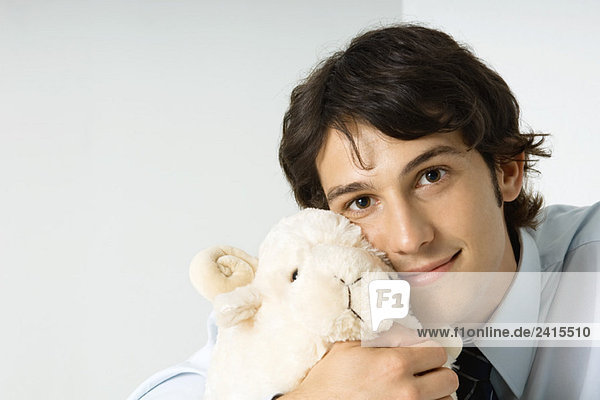 Junger Mann hält ausgestopftes Spielzeug gegen die Wange  lächelnd in die Kamera