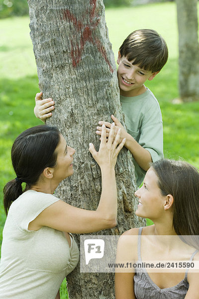 Mutter und Sohn umarmen den Baum  Teenagertochter lächelt ihnen über die Schulter.