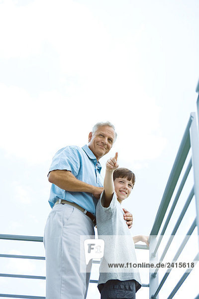Grandfather and grandson standing on balcony  boy pointing  both looking away
