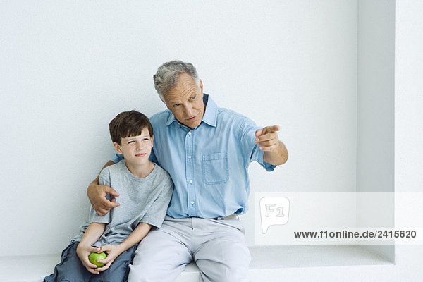 Großvater und Enkel sitzen zusammen  Mann zeigt  Junge hält Apfel