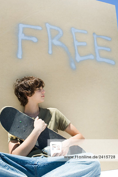 Teenager mit Skateboard und Sprühdose  unter dem Wort'frei' an der Wand'.