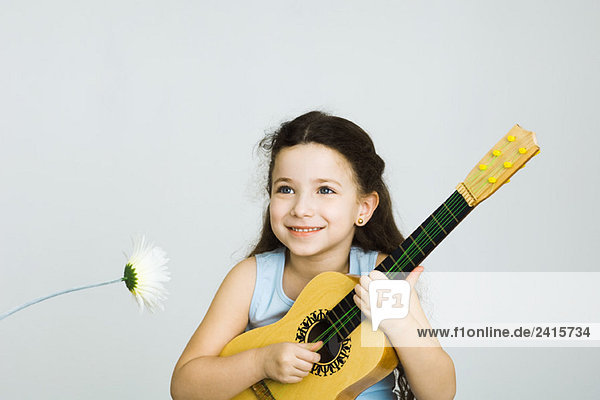 Kleines Mädchen spielt Spielzeuggitarre  neben Blume