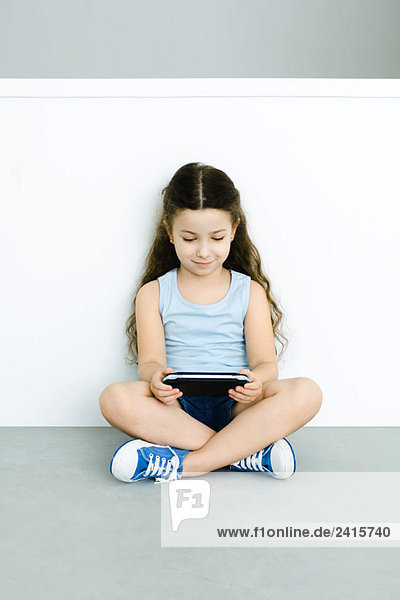 Kleines Mädchen auf dem Boden sitzend  spielt Handheld-Videospiel