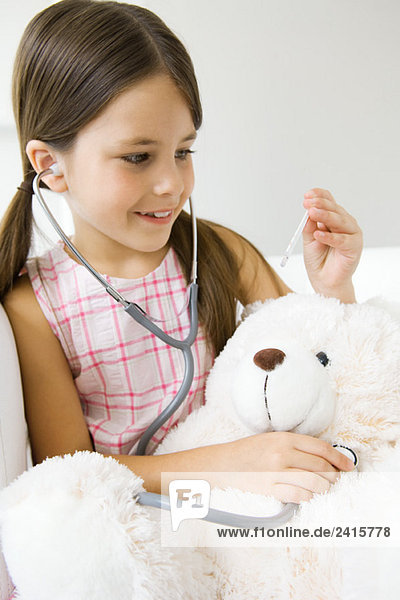 Kleines Mädchen hört Teddys Bärenherz mit Stethoskop  schaut auf Thermometer