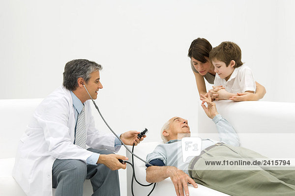 Doctor measuring elderly man's blood pressure  family watching