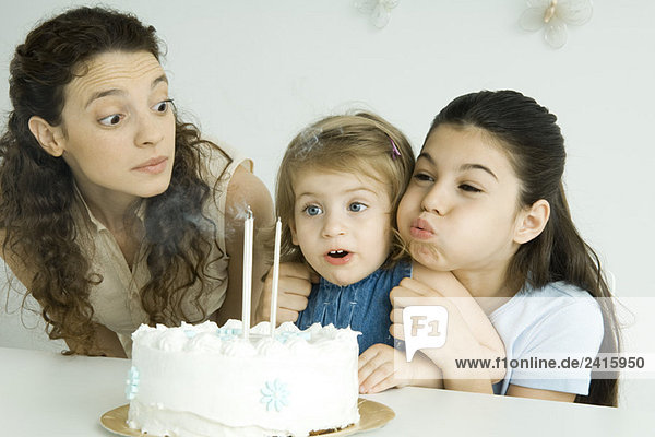 Mädchen hilft jüngere Schwester ausblasen Kerzen auf Geburtstagstorte  Mutter beobachtet