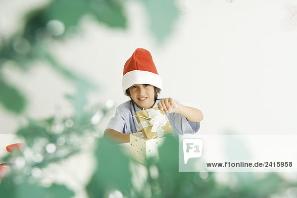 Junge öffnet Weihnachtsgeschenk  trägt Nikolausmütze  lächelt vor der Kamera