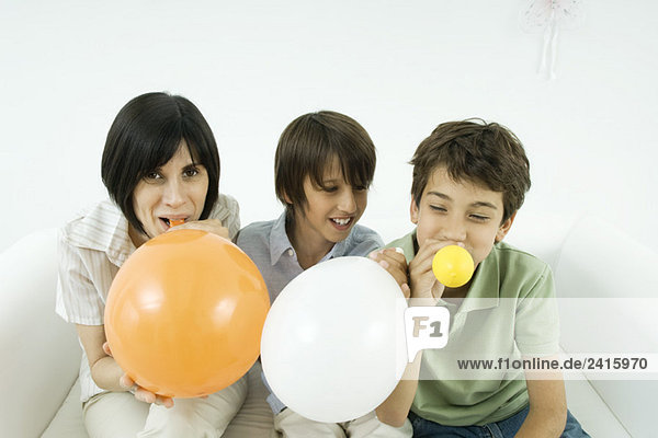Mutter und zwei Söhne  die Luftballons aufblasen  lächelnd  Frau mit Blick auf die Kamera