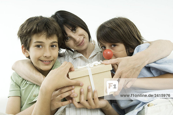 Mutter sitzend mit zwei Söhnen  Geschenk haltend  vor der Kamera lächelnd
