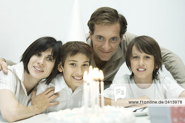 Familie vor Geburtstagskuchen mit angezündeten Kerzen  ein Junge mit Partyhut