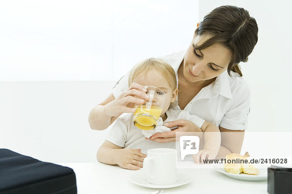 Frau hilft Baby trinken aus Glas Saft