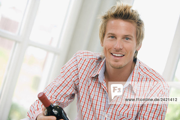 Junger Mann hält eine Weinflasche  lächelnd  Portrait