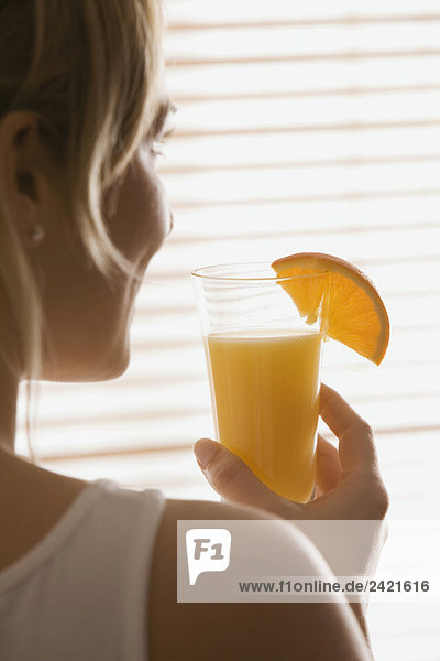 Blonde Frau hält ein Glas Orangensaft  Rückansicht