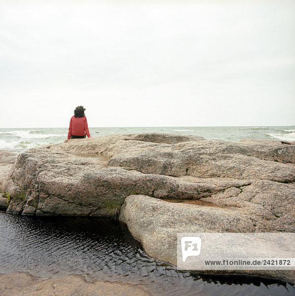 Finnland  Frau am Wasser sitzend  Rückansicht