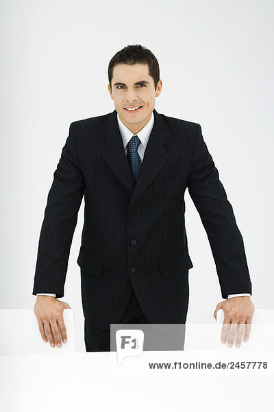 Businessman smiling at camera  standing  hands on chairs  portrait