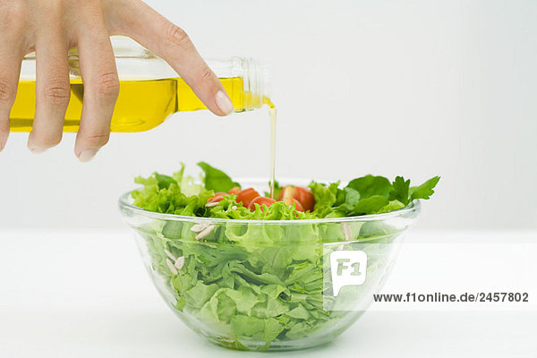 Frau gießt Olivenöl auf Salat  Schnittansicht der Hand