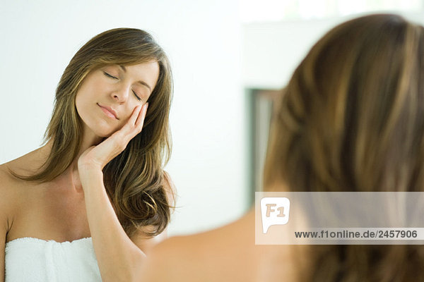 Frau berührt Gesicht  Augen geschlossen  im Spiegel reflektiert