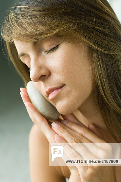 Woman holding smooth stone against face