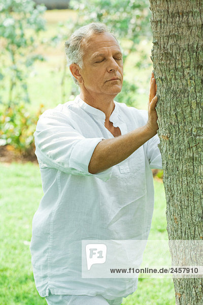 Mature man touching tree trunk  eyes closed