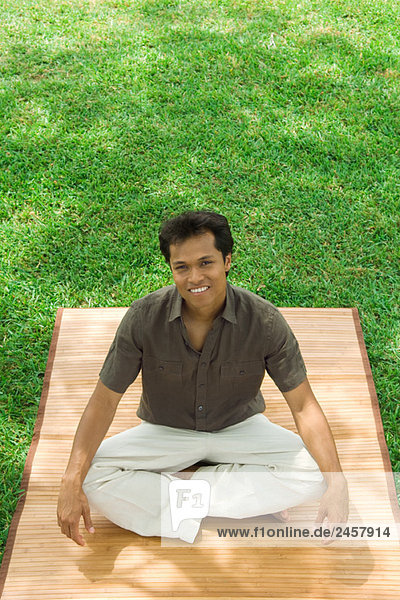 Mann im Schneidersitz im Freien  lächelnd vor der Kamera  hoher Blickwinkel