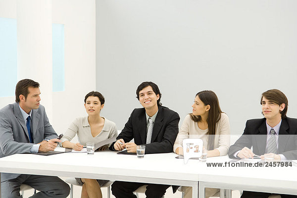 Gruppe von Geschäftspartnern sitzt am Konferenztisch  schaut weg  lächelt