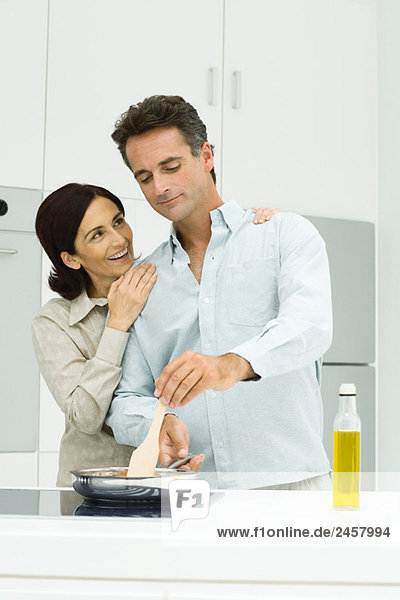 Gemeinsames Kochen in der Küche  Frau legt die Hände auf die Schultern des Mannes.