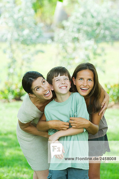 Mother embracing son and teen daughter  all smiling and looking up