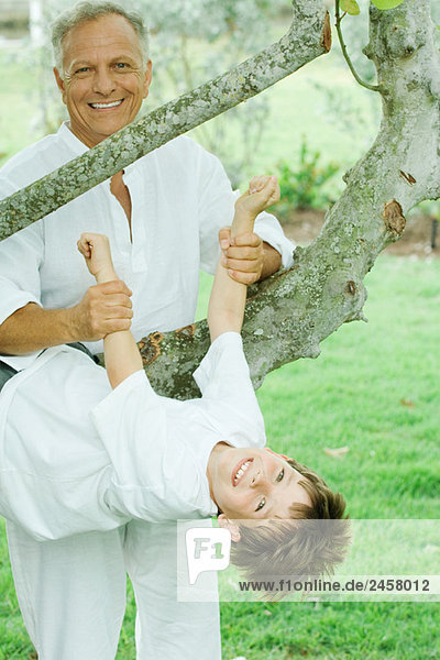 Grandfather holding up grandson hanging from tree  both smiling at camera