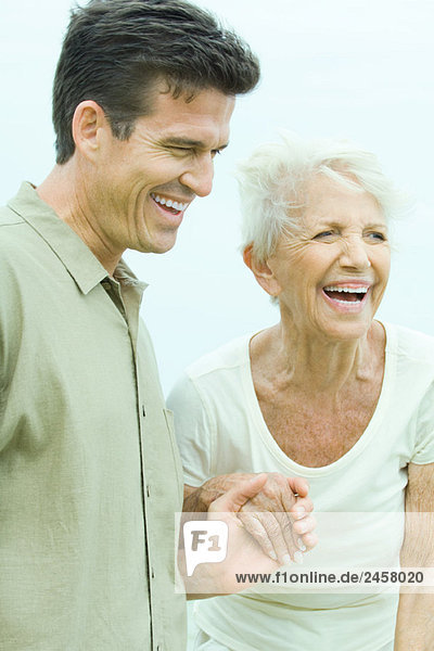 Ältere Frau hält die Hand des erwachsenen Sohnes  beide schauen weg  lächelnd.