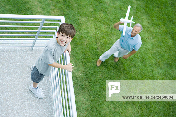 Grandson standing on balcony  grandfather standing below  holding toy airplane  high angle view