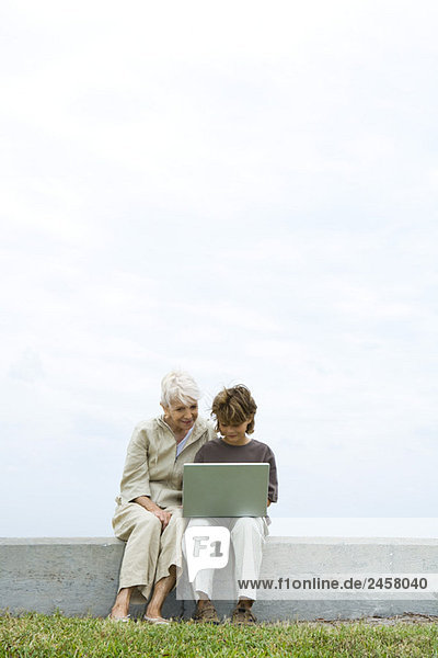 Senior Frau und Enkel sitzen im Freien  mit Laptop-Computer zusammen
