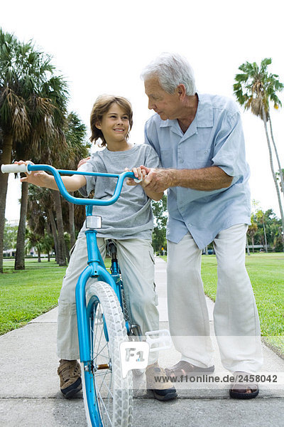 Grandfather teaching grandson to ride bicycle  front view