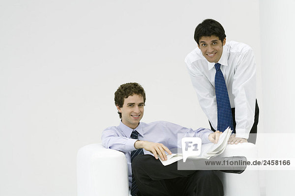 Professioneller Mann sitzend  Zeitung haltend  Kollege über die Schulter gelehnt  beide lächelnd vor der Kamera
