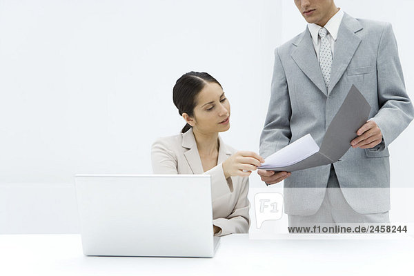 Geschäftsmann zeigt Dokument in der Mappe einer Kollegin  die hinter dem Laptop sitzt  abgeschnittene Ansicht