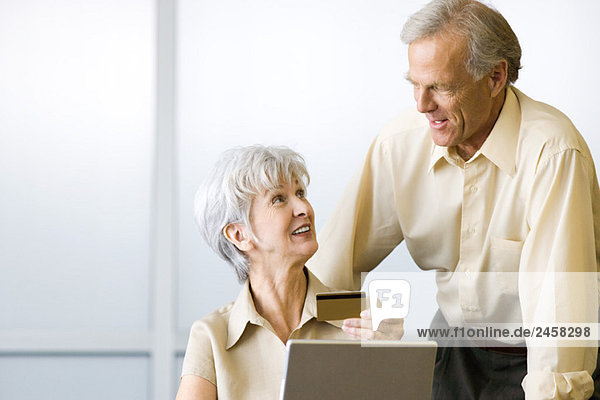 Mature couple looking at each other  woman sitting and holding credit card  man standing