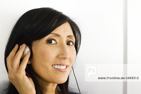 Woman listening to headphones  hand over ear  smiling at camera