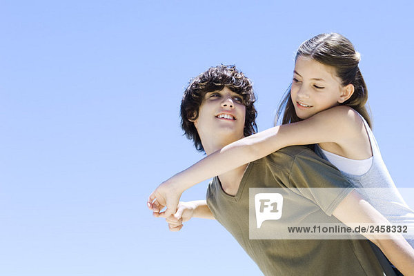 Jugendlicher Junge mit jüngerer Schwester auf dem Rücken  beide lächeln sich an  Blickwinkel niedrig
