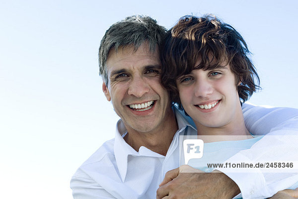 Vater umarmt seinen Sohn von hinten  lächelt in die Kamera  Porträt