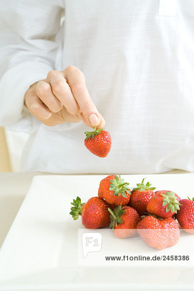 Hand  die eine Erdbeere von einem Stapel auf der Theke aufhebt.