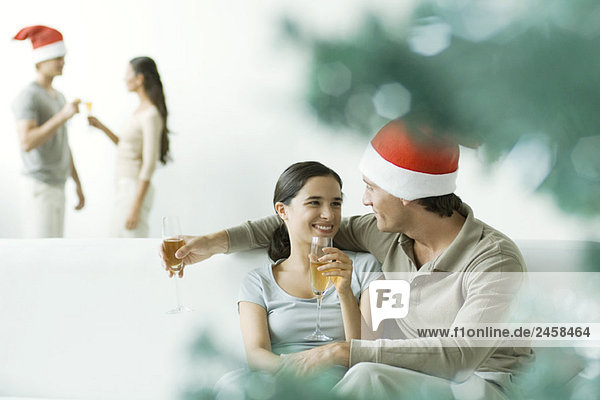 Paar auf dem Sofa sitzend  Champagner trinkend  Mann mit Weihnachtsmütze
