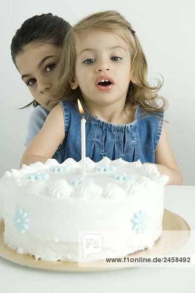 Mädchen bläst Kerze auf Geburtstagskuchen aus  Schwester schaut von hinten in die Kamera