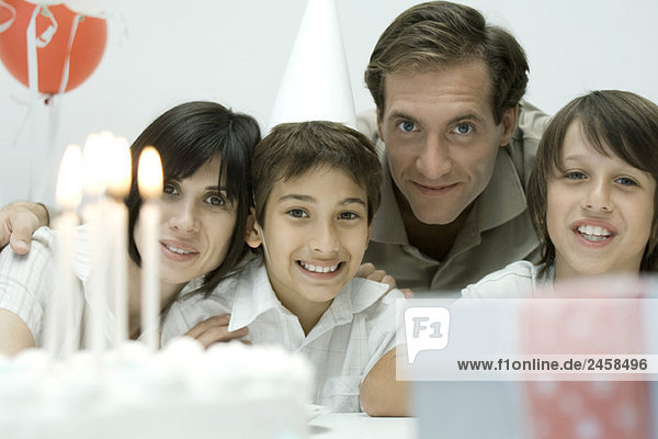 Family in front of birthday cake with lit candles  smiling at camera