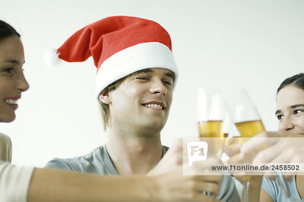 Erwachsene Freunde klirren Champagnergläser  lächelnd  konzentrieren sich auf den Mann mit Nikolausmütze  abgeschnitten