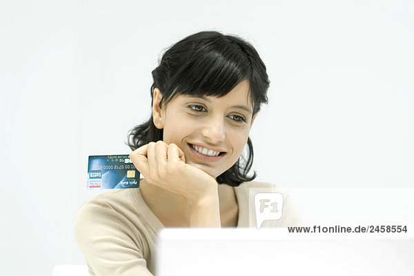 Frau hält Kreditkarte  schaut auf Laptop-Computer  lächelt