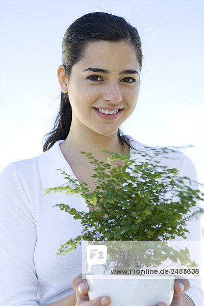 Junge Frau mit Topfpflanze  lächelnd vor der Kamera