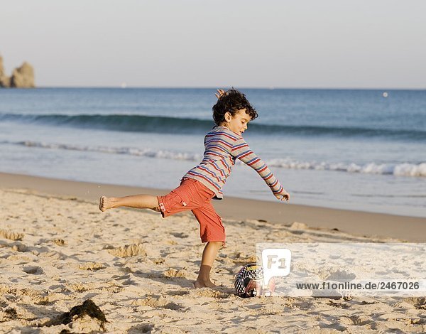 Ein Junge spielen mit einem Ball am Strand Portugal.